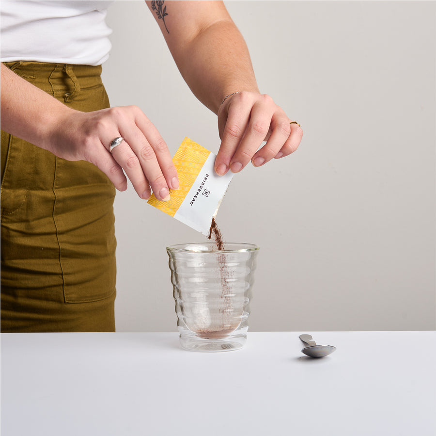 someone pouring a package of instant coffee into a clear cup 