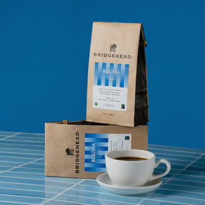Two bags of Bolivia coffee stacked, next to a cup of coffee
