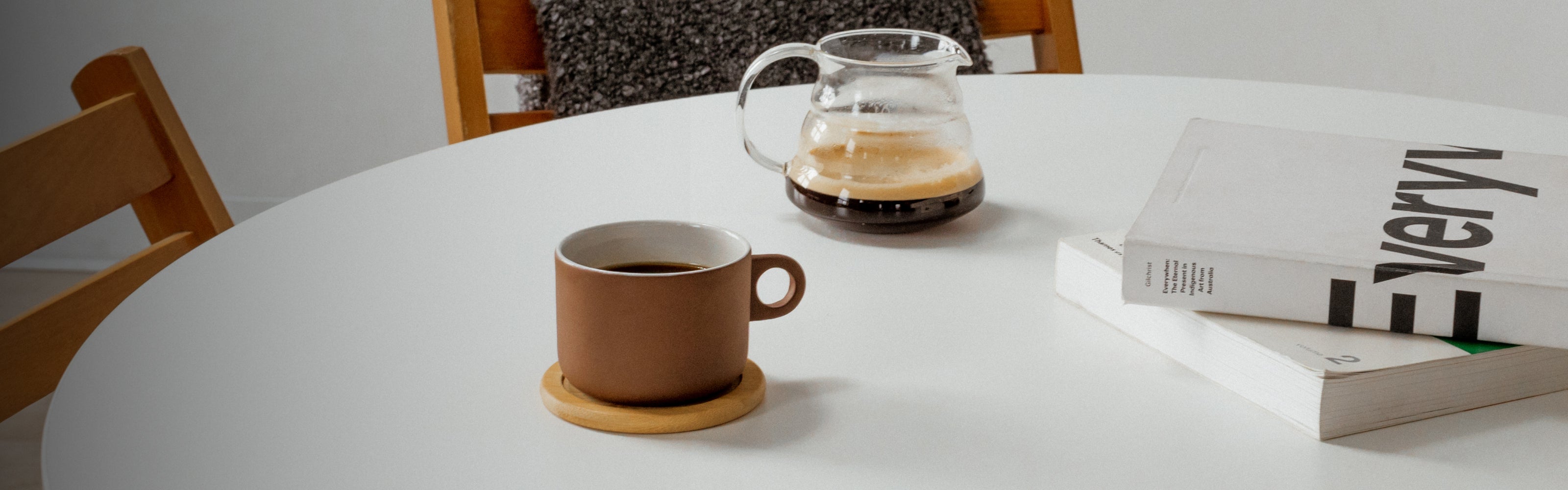 Brown mug on a white table with a coffee carafe and books in the background