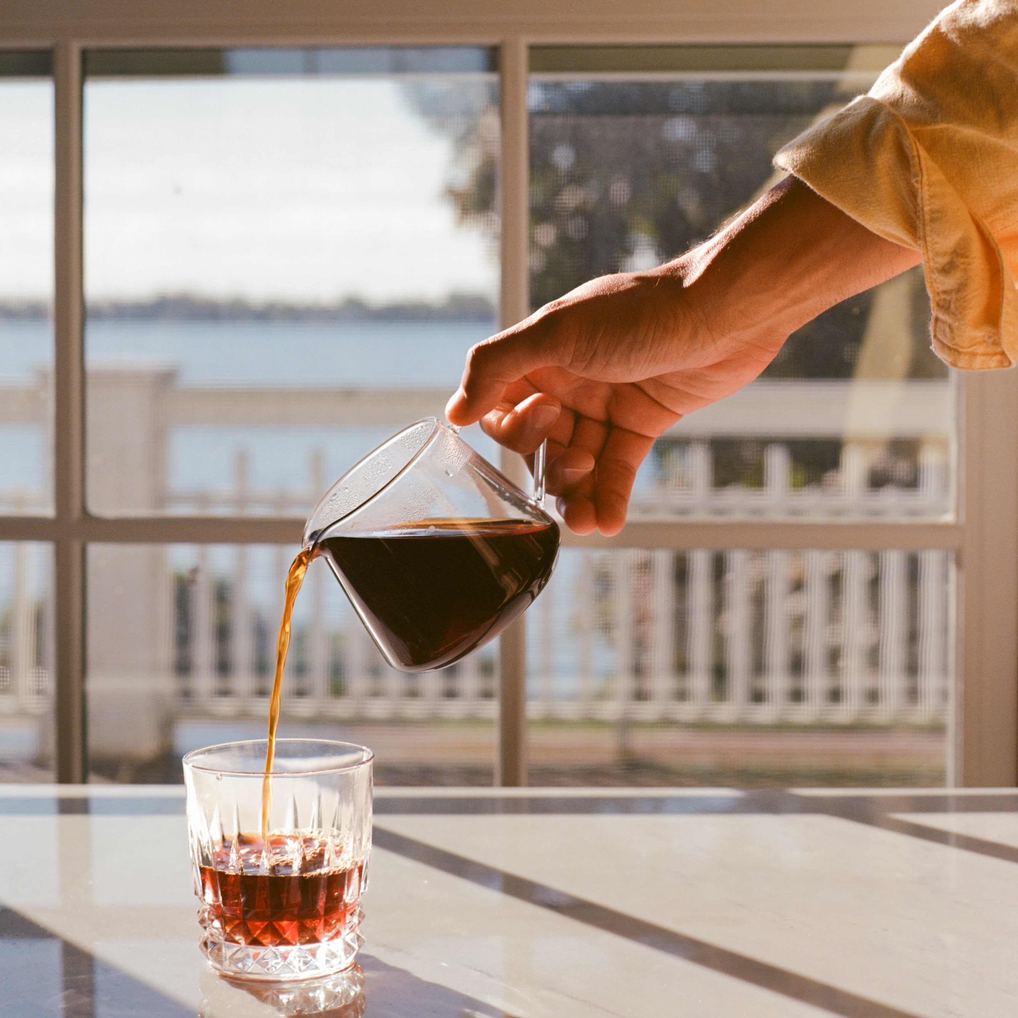 Someone pouring coffee into a clear glass