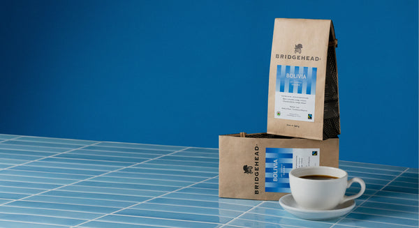 two 12oz bags of Bolivia coffee stacked, next to a cup of coffee