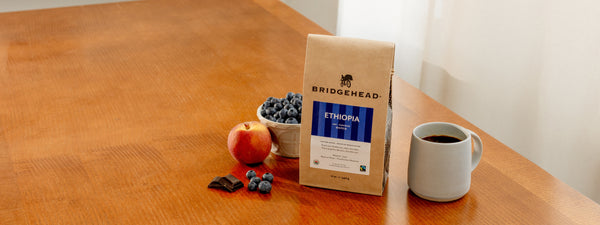 12oz bag of Ethiopia coffee bag, next to blueberries, a peach, some chocolate, and a mug of coffee